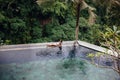 Slim brunette woman in swimsuit relaxing on edge tropical infinity pool in jungle. Palms around and crystal clean Royalty Free Stock Photo