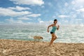 Slim sporty girl running with a dog on the beach in sunlights. Leisure outdoor activities, enjoying life. Healthy lifestyle Royalty Free Stock Photo