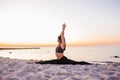 Slim strong young woman in black practicing yoga doing the splits on sand beach close-up with copy space. Sunset, summer. Healhy