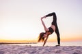 Slim strong young woman in black practicing yoga doing the splits on sand beach close-up with copy space. Sunset, summer. Healhy