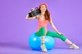 Slim student girl sits on fit ball with portable cassette player waiting to start the retro 80s dance party