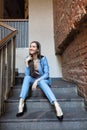 Slim stylish girl with long hair wearing blue suit sitting on the stairs. Ladies fashion and footwear in summer city. Royalty Free Stock Photo