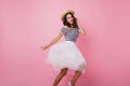 Slim stylish latin lady in hat dancing on pastel background. Cheerful tanned girl in lush skirt foo