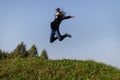 Slim teen girl jumping high over green grass against the sky.