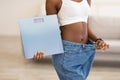 Slim Woman Holding Scales Wearing Large Jeans After Slimming Indoors Royalty Free Stock Photo