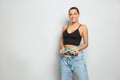 Slim woman in oversized jeans with measuring tape on light background, space for text