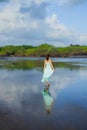 Slim woman walking barefoot on empty beach. Full body portrait. Caucasian woman wearing long dress. View from back. Water Royalty Free Stock Photo