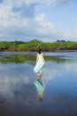 Slim woman walking barefoot on empty beach. Full body portrait. Caucasian woman wearing long dress. View from back. Water Royalty Free Stock Photo