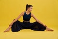 Female yogi doing stretching exercise sitting with legs wide apart indoors.