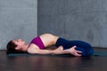 Slim young woman lying in Supta Virasana, reclining Hero Pose, stretching abdominal and back muscles on mat in gym