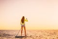 Slim young woman on stand up paddle board with beautiful sunset or sunrise colors Royalty Free Stock Photo