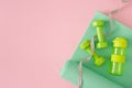 Top view photo of dumbbells green exercise mat bottle of water and tape measure on pastel pink background