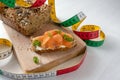 Slimming with low carb or ketogenic diet, protein bread with tape measure and a sandwich with salmon and herb garnish on a cutting Royalty Free Stock Photo