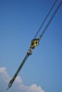 Slings and yellow hook of a construction crane against a blue sky and white cloud. The symbolism of construction and creation