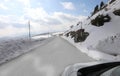 slippery mountain road with snow on the sides and posts to mark the limit of the roadway seen from inside a car