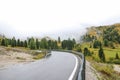 Slippery wet road with high mountains covered with fog, yellowing grass, and green tress around Royalty Free Stock Photo