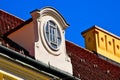 sloped red clay tile residential roof with decorative dormer. oval wood window. yellow stucco ornate chimney.