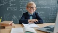 Slow motion of prodigy kid in university classroom at desk with chalkboard in background