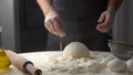 Baker pours flour on dough for pizza and claping hands with flour. Baker sprinkles pinch of flour