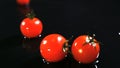 Slow motion of tomatoes falling with water drops on black surface.