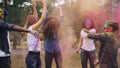 Slow moton of joyful men and women enjoying Holi colors festival jumping, laughing and throwing colorful powder on lawn