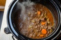 slowcooker with beef stew simmering, top view steam visible