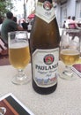 A glass bottle of Paulaner Original MÃ¼nchner Hell beer is placed on a table alongside two partially filled beer glasses Royalty Free Stock Photo
