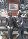 Bronze statues of two men seated on a metal bench in a casual and engaging pose Royalty Free Stock Photo