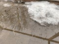 Slushy white snow patch on sidewalk with icy puddles and visible tree reflections indicating winter thaw and melt process in cold Royalty Free Stock Photo
