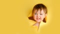 A sly baby in a hole on a paper yellow background. Torn child\'s head st Royalty Free Stock Photo