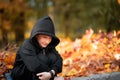 Sly boy in a black hooded jacket sits on the curb and smiles Royalty Free Stock Photo