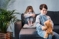 Sly boy holding teddy bear while offended girl sitting on sofa Royalty Free Stock Photo