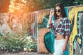 Slylish woman in sunglasses posing near graffiti wall. sunlight background