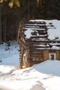 A smal and oldl wooden house in a snowy forest.