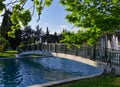 Smal pedestrian bridge leading to small island inside a park lake. Sycamore tree leaves blue sky. Alsos Filadelfeias, Athens,