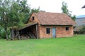 Small abandoned red brick house with broken windows and doors next to old destroyed wooden garage surrounded with grass and trees Royalty Free Stock Photo