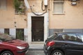 Small access portal door to an old basement apartment building with barred windows and some plants