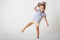 Small adorable female child has funny expression, two pony tails, wears casaul t shirt and shorts, stands on one leg, poses agains Royalty Free Stock Photo