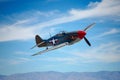 A small airplane is seen flying through a clear blue sky, with white fluffy clouds below, A vintage World War II fighter aircraft Royalty Free Stock Photo