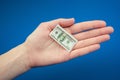 Small American dollar bill in hand on a blue background Royalty Free Stock Photo