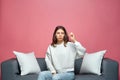 Small amount gesture. Sad dissapointed modern young girl showing little size by fingers sitting on sofa