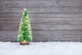 small artificial green christmas tree with holiday lights on snow against wooden rustic background Royalty Free Stock Photo