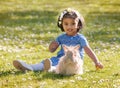 A small Asian girl is sitting with home rabbit on green grass in spring day