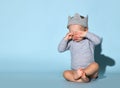 Small baby boy in jumpsuit, decorative crown on head and barefoot sitting on floor, touching eyes and crying or feeling sleepy