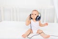 Small baby boy 8 months old sitting on the bed in the children`s room with headphones and listening to music, place for text Royalty Free Stock Photo