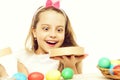 Small baby girl or cute child with happy face and rabbit pink ears on blonde head around colorful easter eggs holding