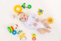 Small baby girl 6 months old lying on her back on a white bed at home among toys, top view Royalty Free Stock Photo