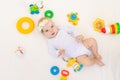 Small baby girl 6 months old lying on her back on a white bed at home among toys, top view Royalty Free Stock Photo