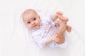 A small baby girl 6 months old is lying on a light bed in a beautiful white bodysuit and smiling at the camera, the baby is lying Royalty Free Stock Photo