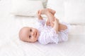 A small baby girl 6 months old is lying on a light bed in a beautiful white bodysuit and smiling at the camera, the baby is lying Royalty Free Stock Photo